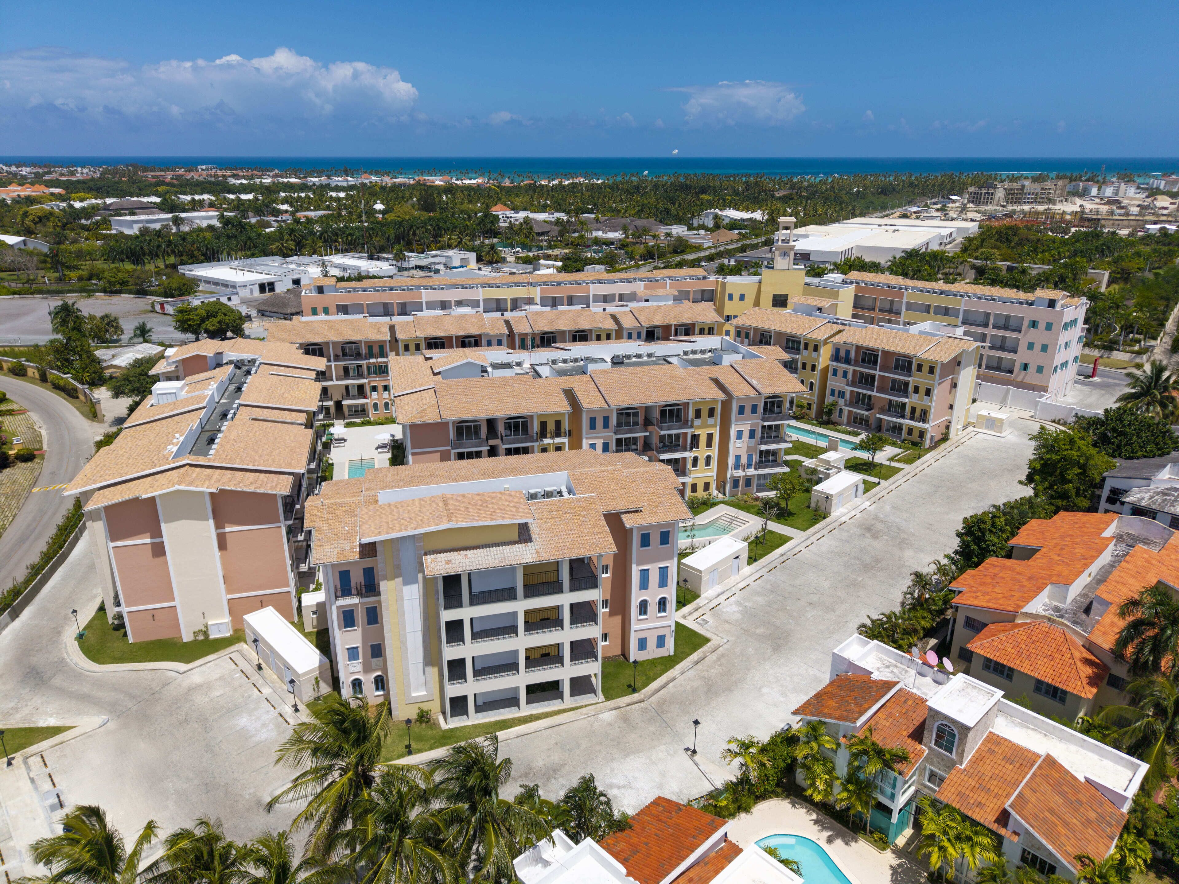 A multi-story residential building with a central courtyard, surrounded by palm trees and a view of the ocean.