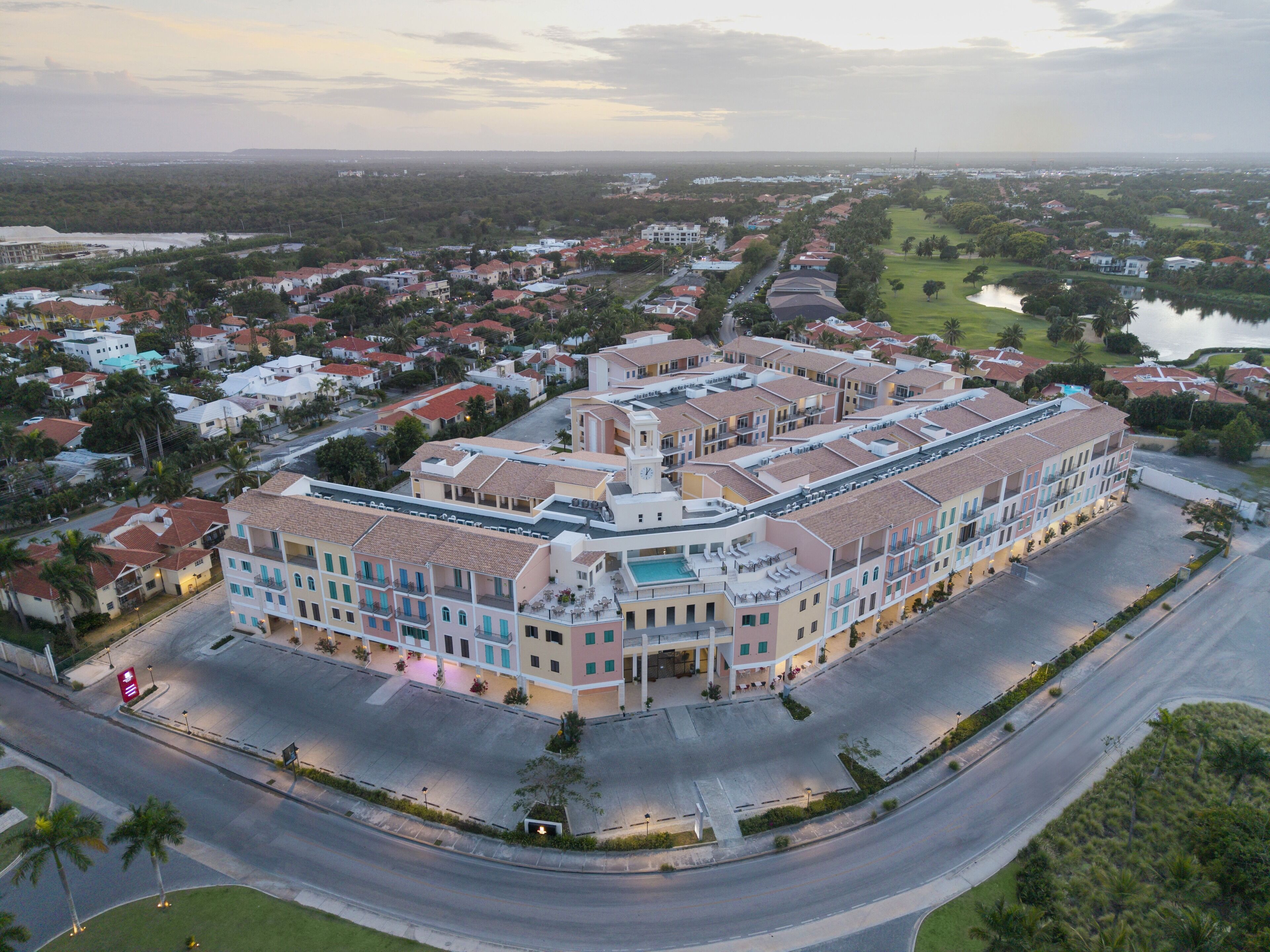 Un grand hôtel à plusieurs étages, doté d’une cour intérieure, entouré d’un quartier résidentiel et bordé par un plan d’eau.