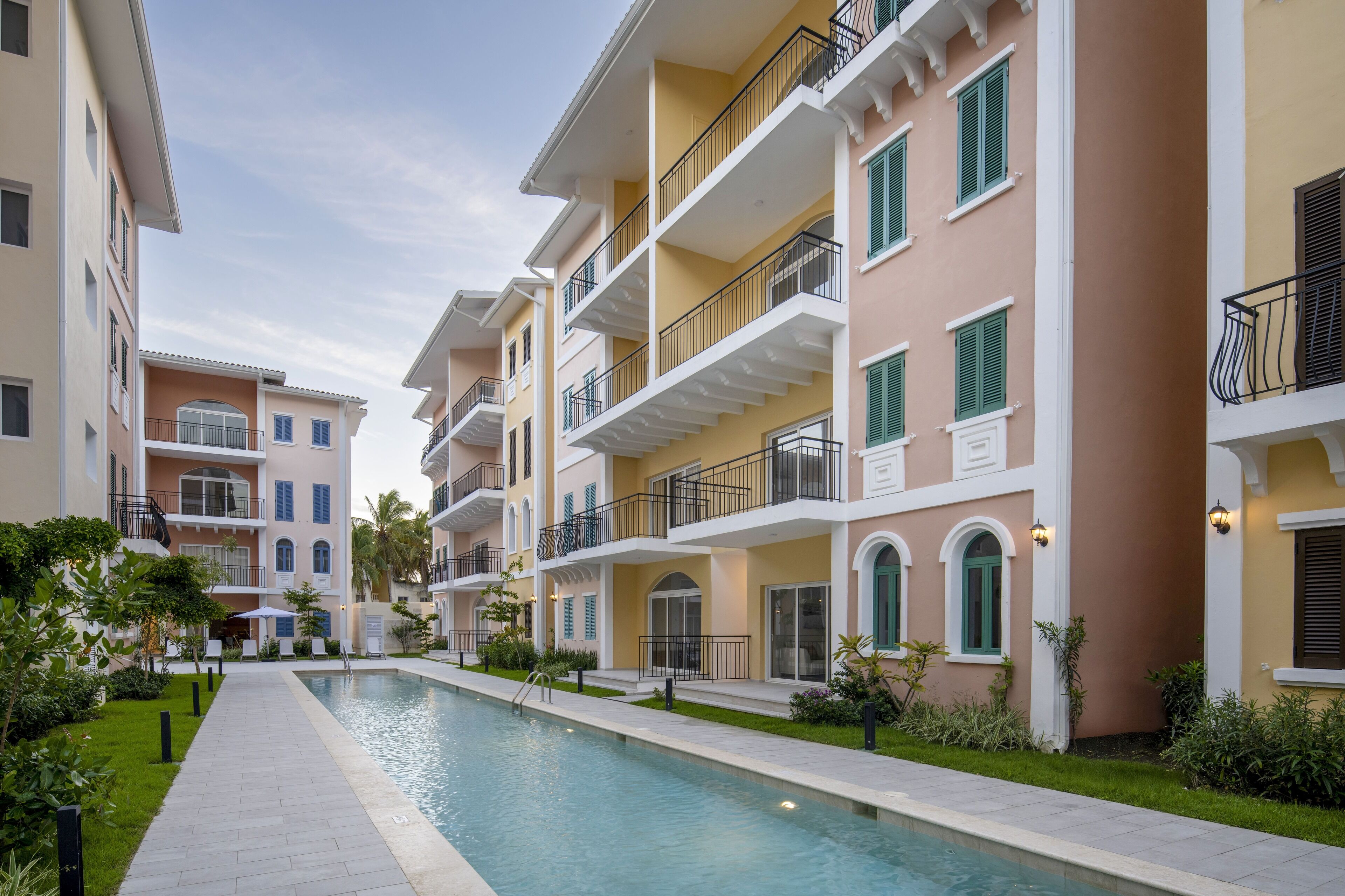 A pool area with a pathway, surrounded by multi-story buildings with balconies and green shutters.