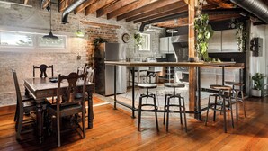 A rustic kitchen with exposed beams, a brick wall, and a wooden dining area with a table and chairs.
