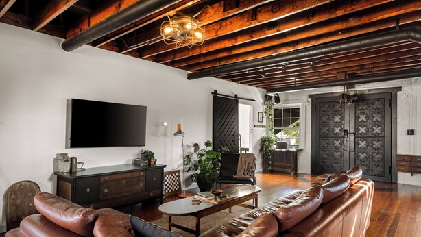 A spacious living room with a leather sofa, a coffee table, and a TV mounted on the wall.