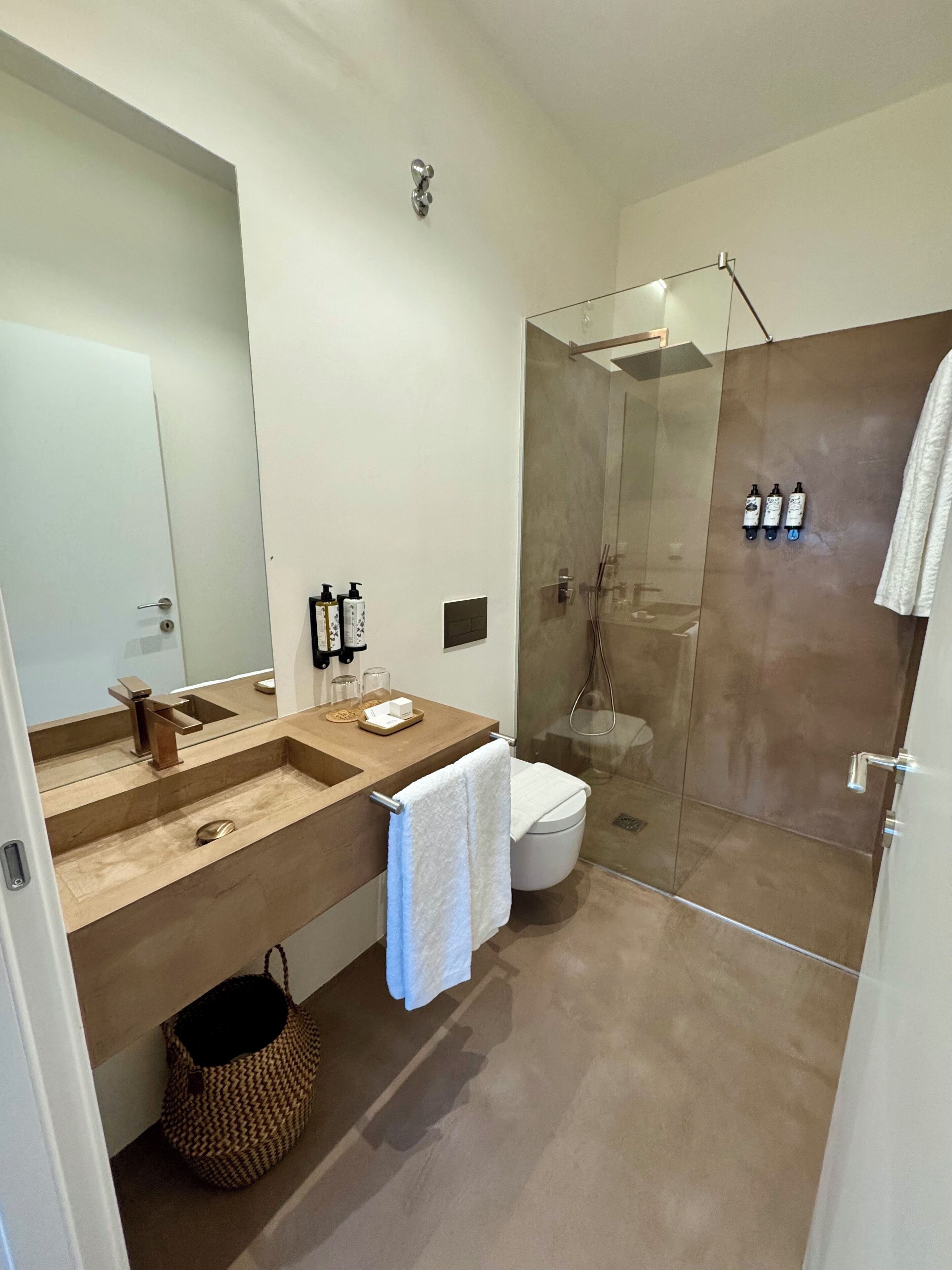 A modern bathroom with a large mirror, a wooden vanity, a glass shower enclosure, and a white toilet.