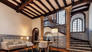 A spacious living room with a high wooden ceiling, a staircase with ornate railings, and a view of the upper floor. - CICIOSO Boutique Hotel (Évora)