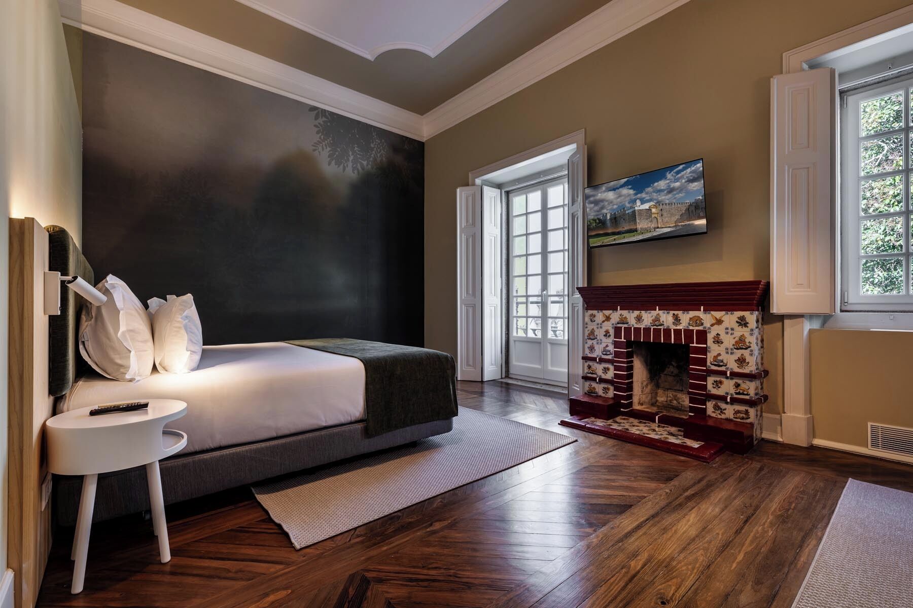 Un dormitorio con cama, chimenea, televisor y un ventanal grande.