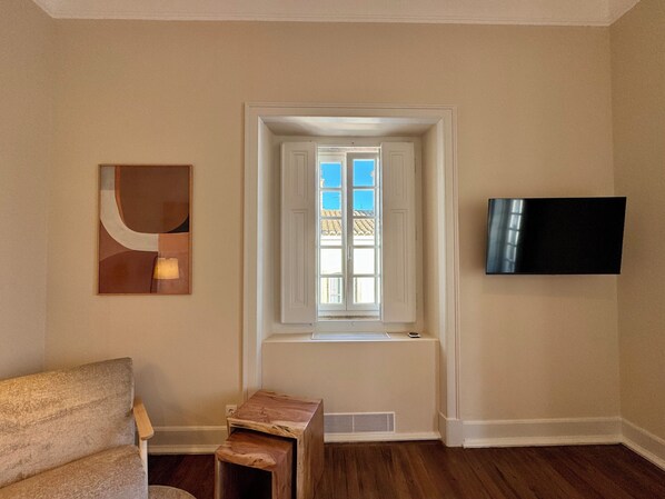 Una habitación con ventana, un televisor de pantalla plana en la pared y un taburete de madera.