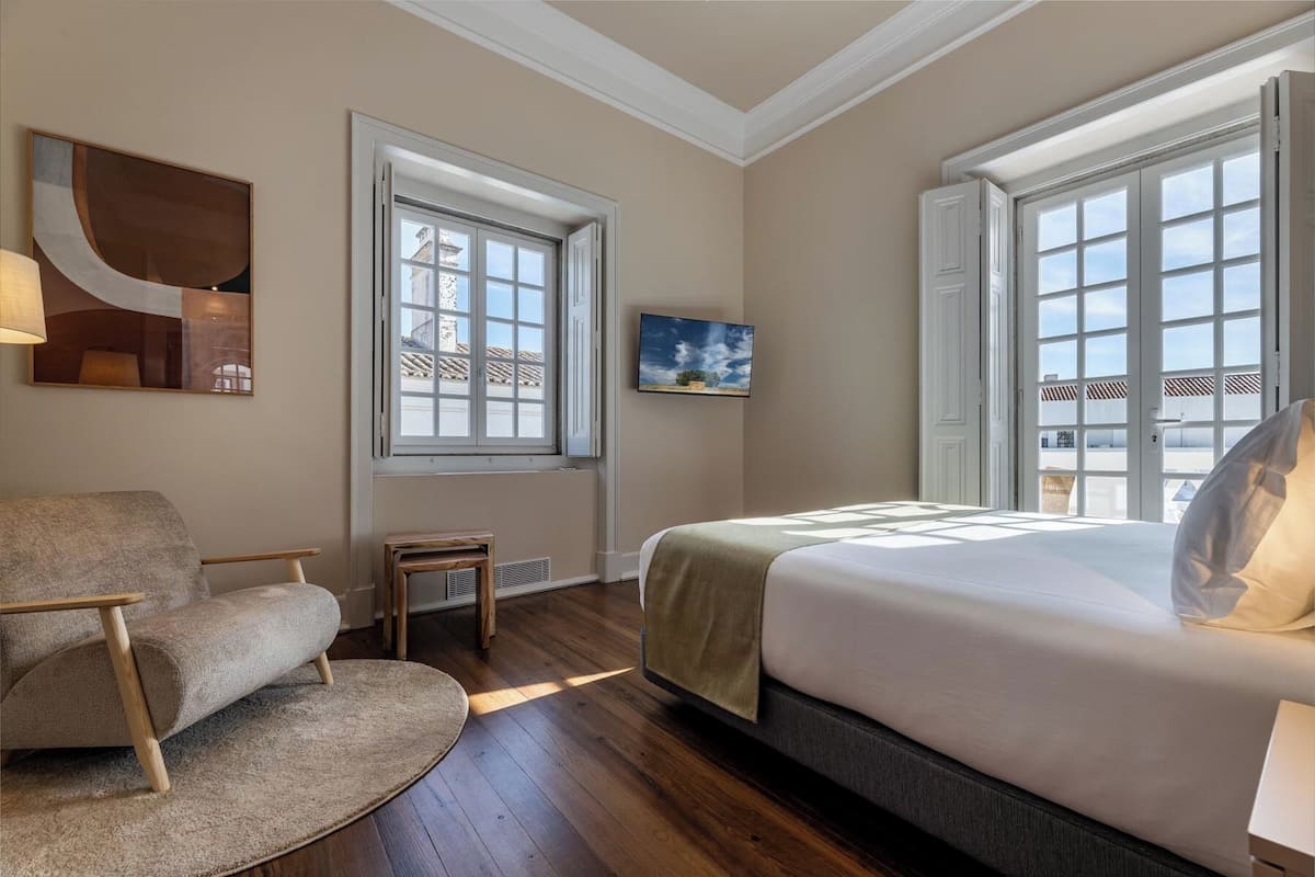 Un dormitorio con una cama grande, una silla, una mesita y un televisor en la pared.