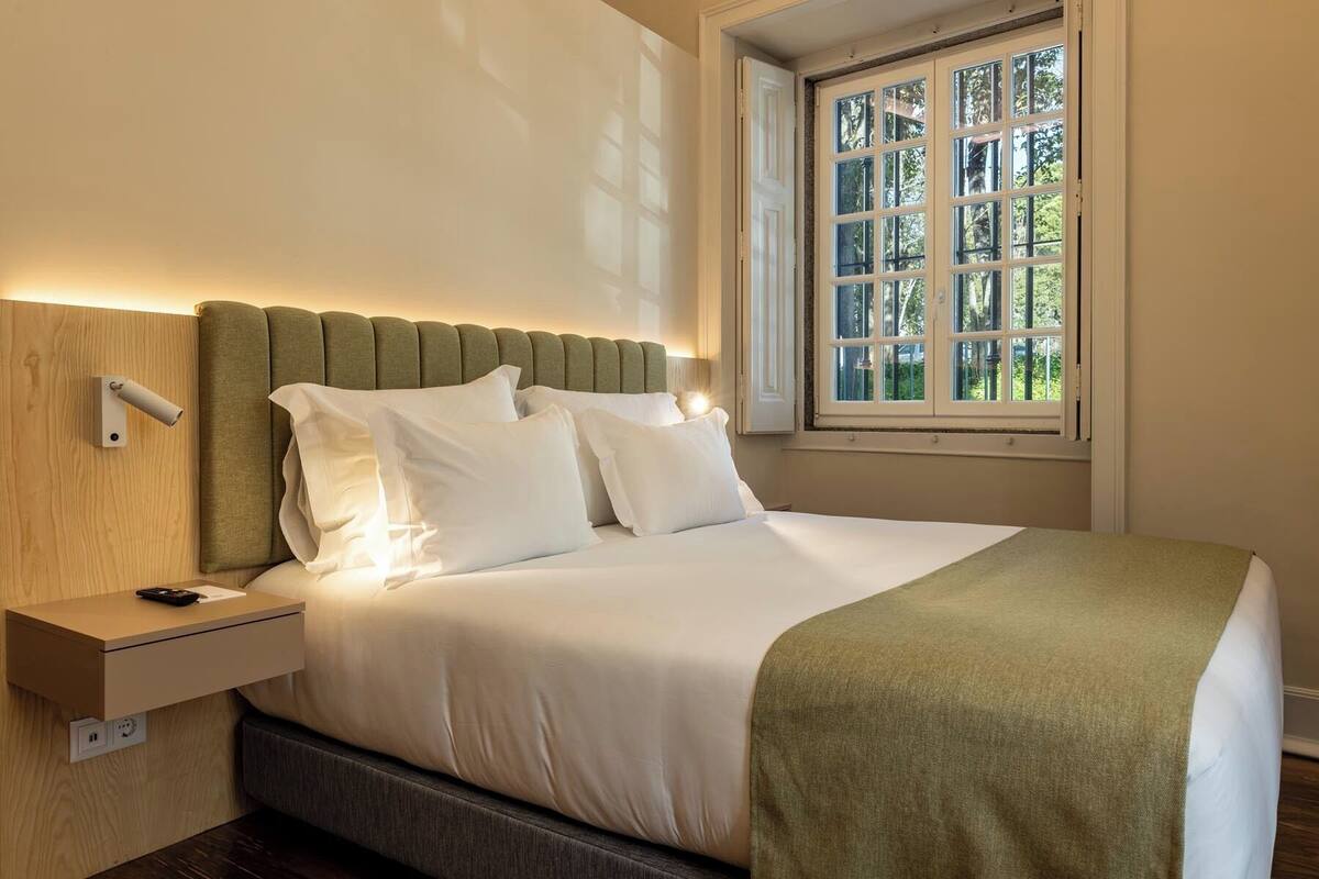 Una cama bien hecha con sábanas blancas, un plaid verde y un cabecero contra la pared.