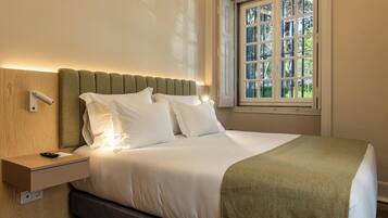 A neatly made bed with white linens, a green throw blanket, and a headboard against a wall.