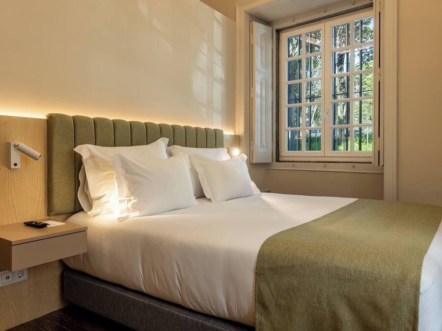 A neatly made bed with white linens, a green throw blanket, and a headboard against a wall.