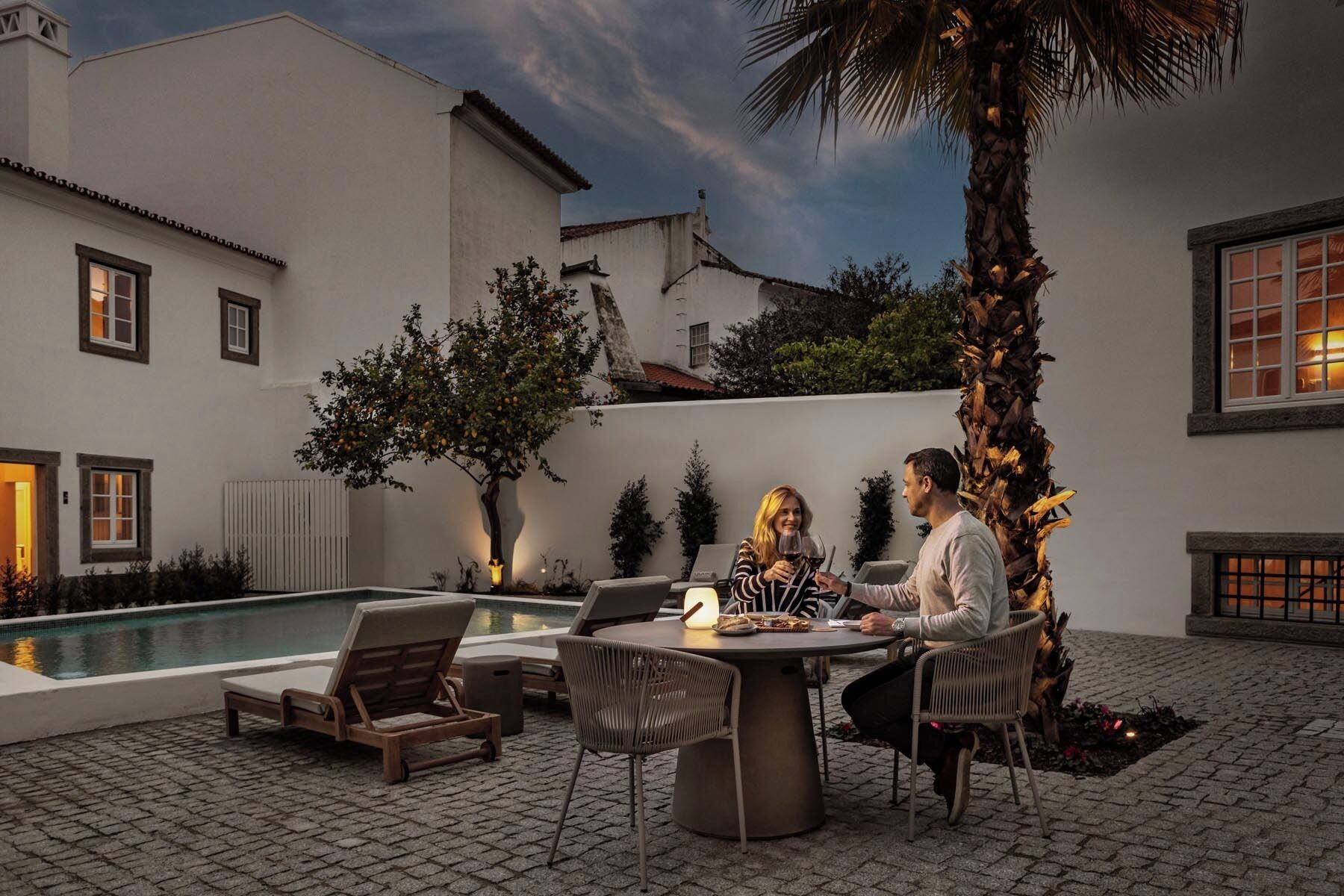 A poolside area with a table and chairs, a pool, and a palm tree.