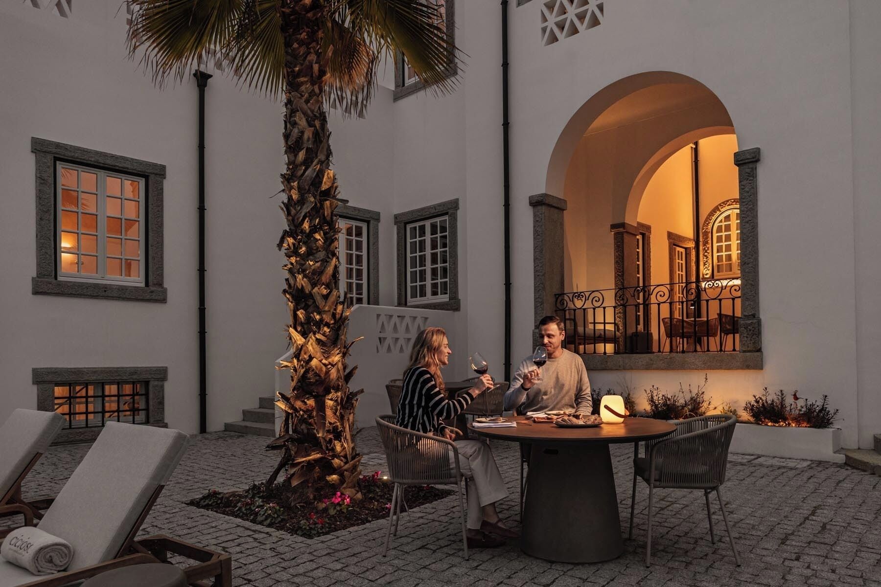 Una pareja sentada en una mesa al aire libre con vista al interior de un edificio a través de un arco.