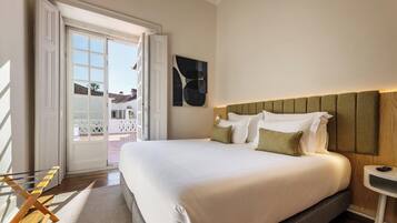 Habitación de hotel con una cama grande, cabecera de madera, una mesita de noche pequeña y vistas a un área exterior a través de una puerta abierta.