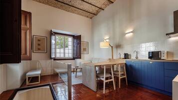 A compact kitchen with a wooden table, blue cabinets, and a window with open shutters.