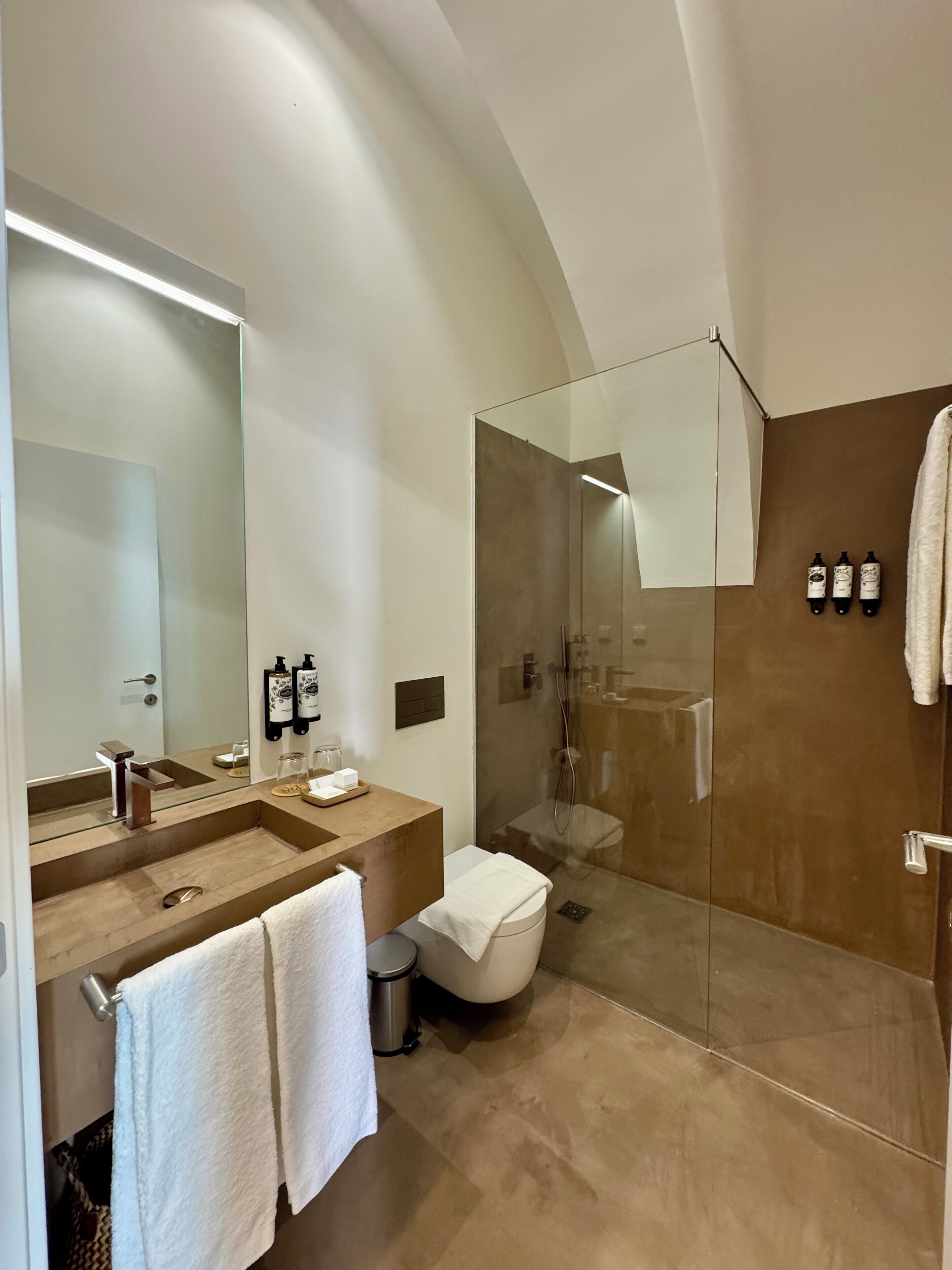 A modern bathroom with a glass-enclosed shower, a large mirror, and a beige vanity.