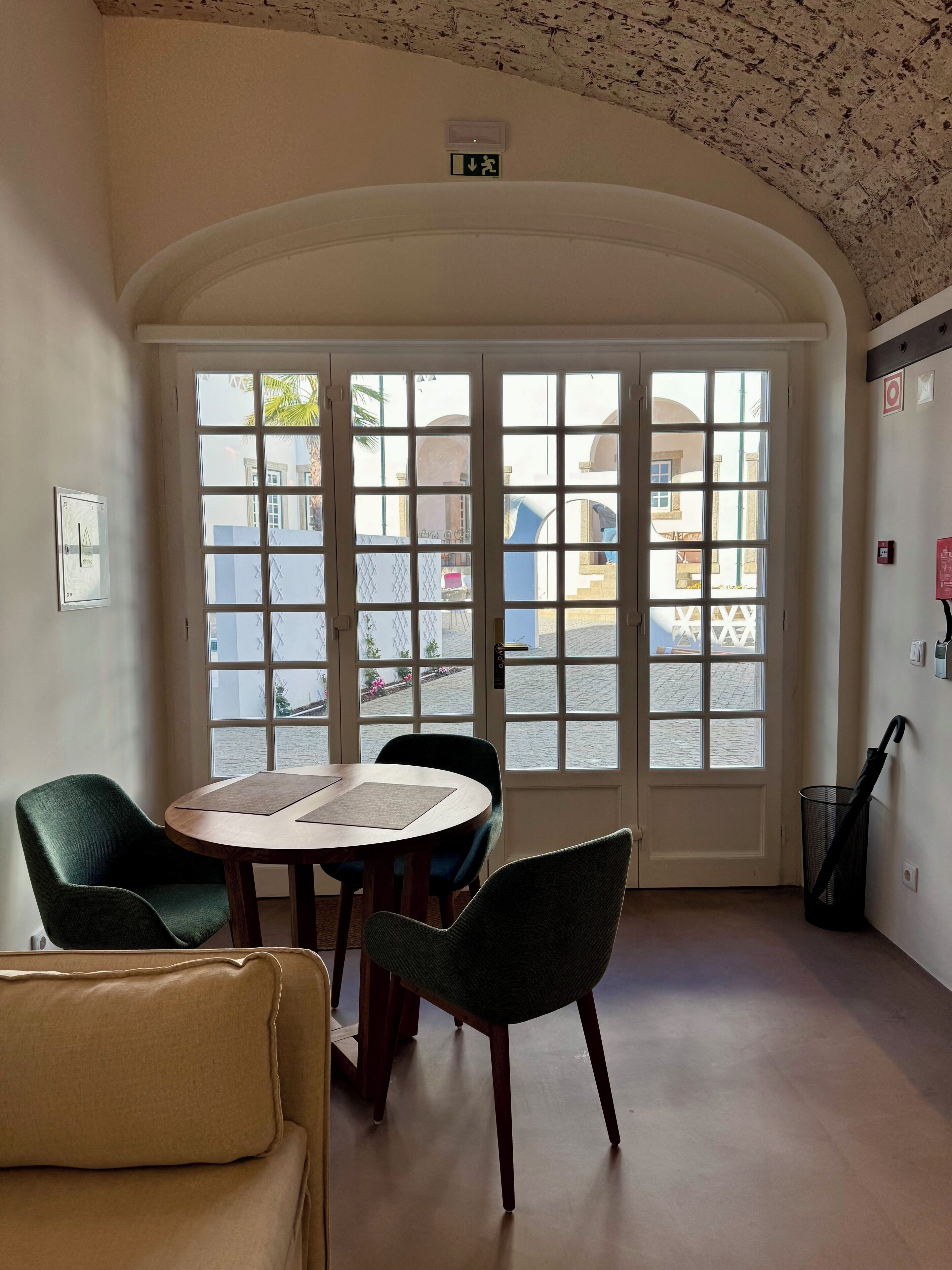A room with a round table, four chairs, a sofa, and a large arched window with a view of the street.