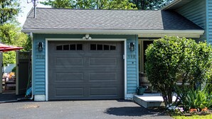 A residential garage with a grey door, number 198, and a small garden with a tree and plants.