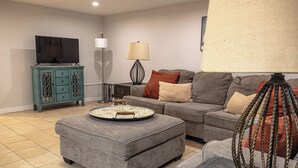 A living room with a grey sofa, ottoman, and a television on a cabinet.
