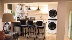 A modern kitchen with bar stools, a coffee machine, and a washing machine.