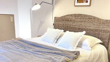 Un lit bien fait, avec une couverture à rayures, une tête de lit en osier et un tableau encadré accroché au mur.