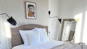 A bedroom with a large bed, a round wooden table, a wicker headboard, a framed artwork, and a mirror. - Jeanne's apartment. 500 from the castle, in a quiet, green setting (Chinon)