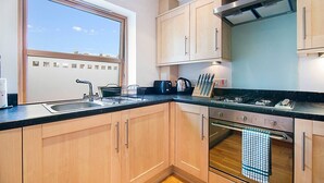 Una cocina moderna con armarios de madera, encimera negra, un fregadero, una estufa y una ventana con vistas a la ciudad.