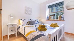 Un dormitorio ordenado con cama, lámparas de noche, ventana con vistas y un estante con toallas.