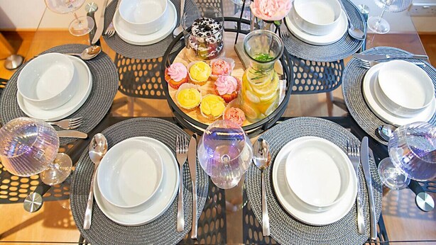 Mesa dispuesta para seis personas, con platos, cubiertos y vasos, rodeada de sillas.