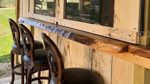 A wooden bar area with a large window, two chairs, and a bench. - Cozy Cabin (New Lexington)