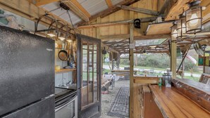 A rustic kitchen with a large refrigerator, wooden cabinets, and a dining area with outdoor seating. - Cozy Cabin (New Lexington)