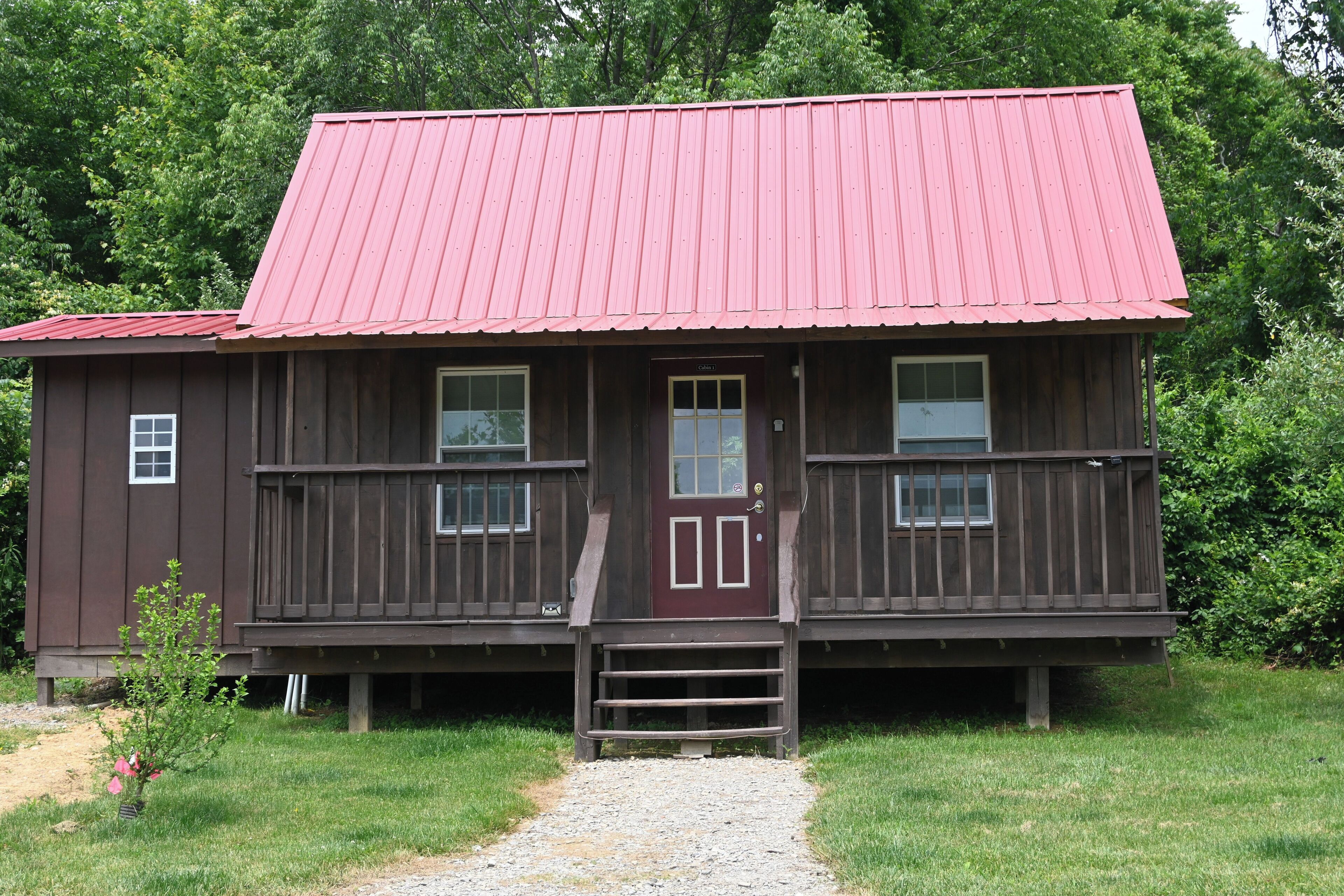 A wooden cabin with a red roof, a front porch, and a gravel path leading to the door.