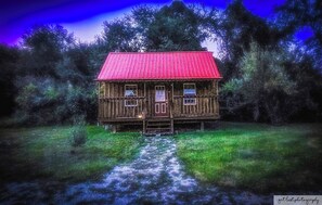 Una cabaña de madera rústica con techo rojo, rodeada de un bosque denso.