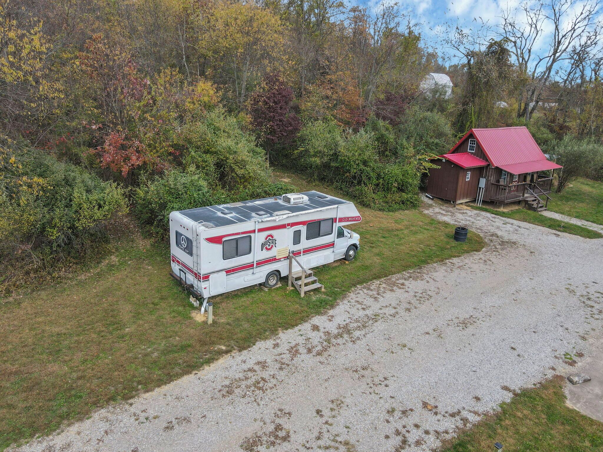A recreational vehicle (RV) parked on a gravel path with a red-roofed cabin nearby.