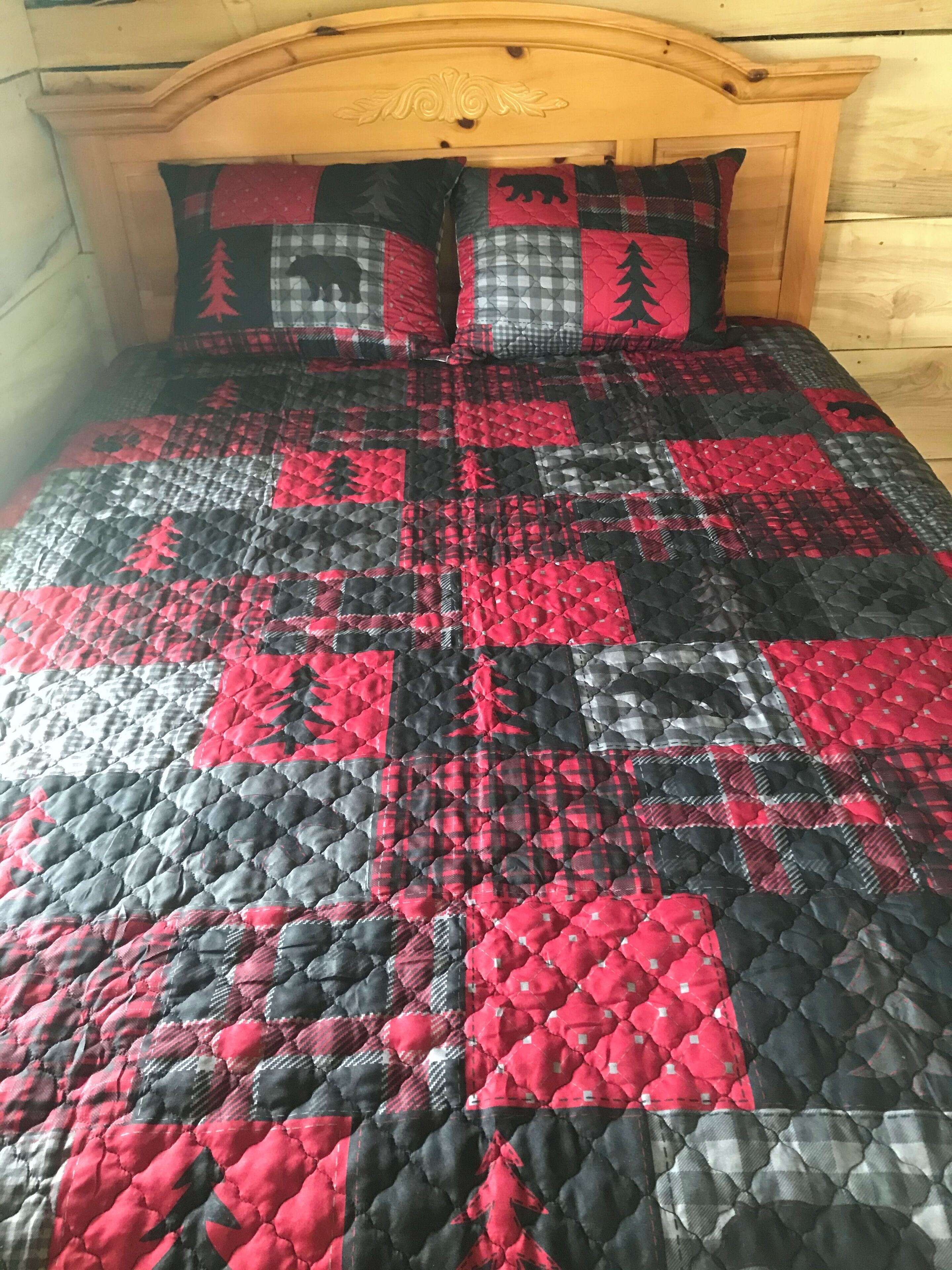 A bed with a quilt featuring a red and black pattern.