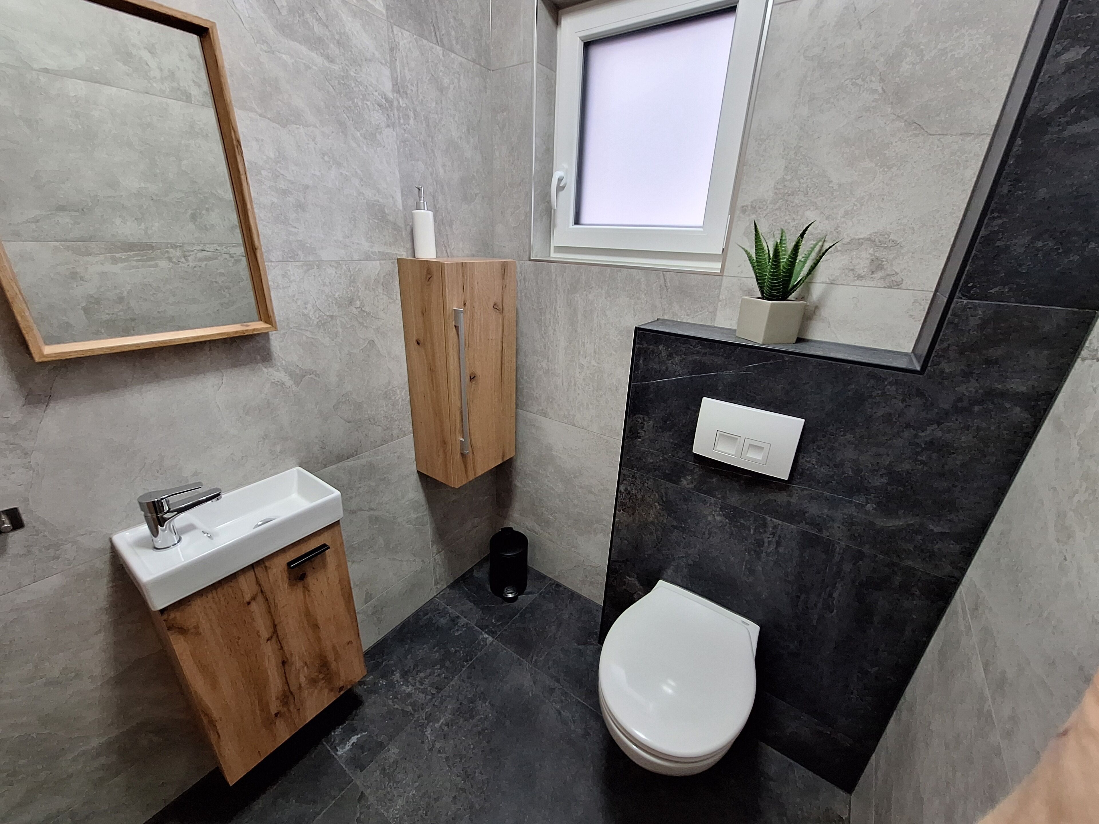 Et moderne badeværelse med en trækommode, et hvidt toilet, et lille vindue og en potteplante.