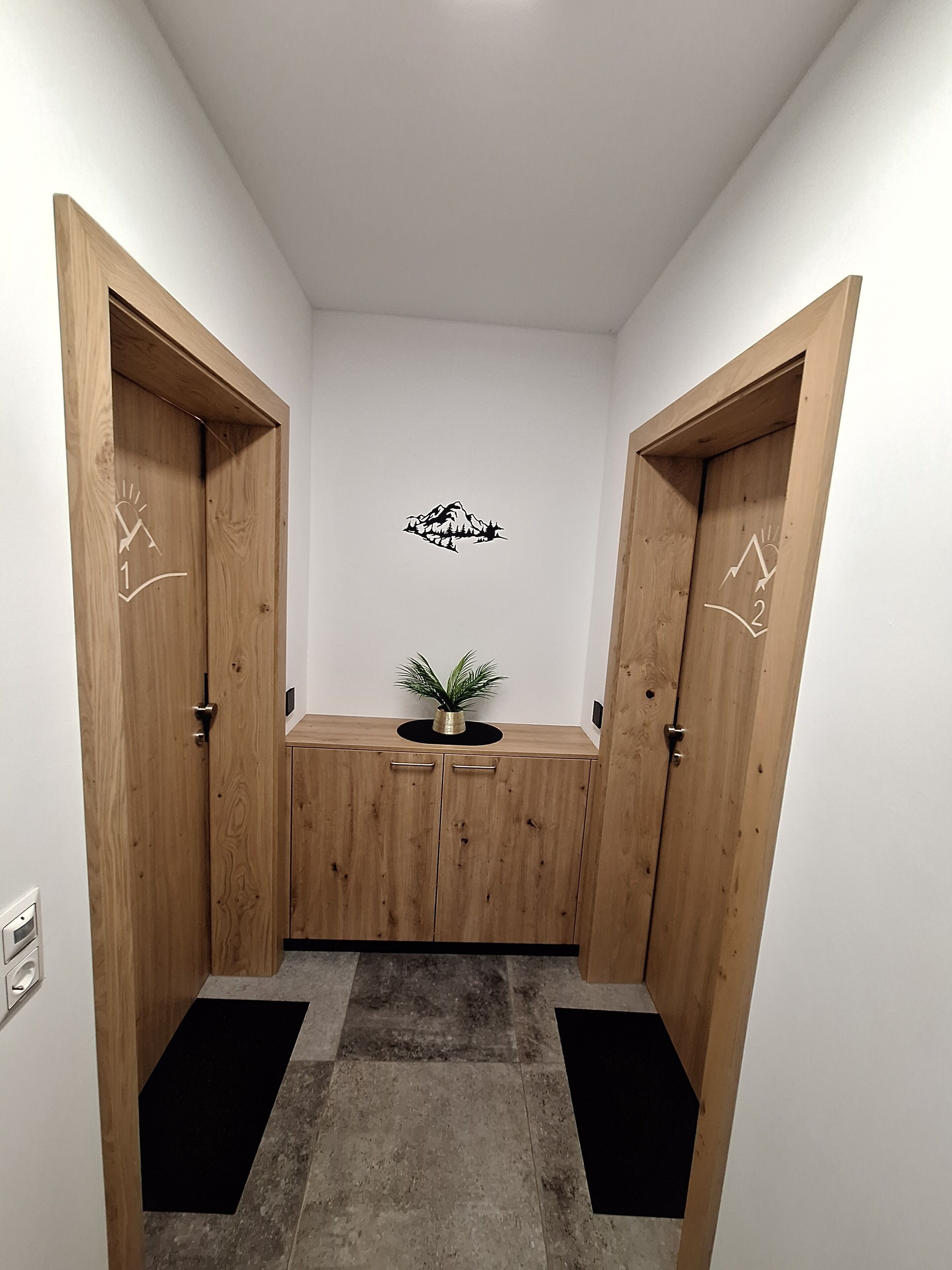 A hallway with wooden doors, a small plant on a black table, and a wall decal.