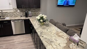 Une cuisine moderne dotée d’un plan de travail en granit, de meubles de rangement aux couleurs sombres et d’un lave-vaisselle encastré.