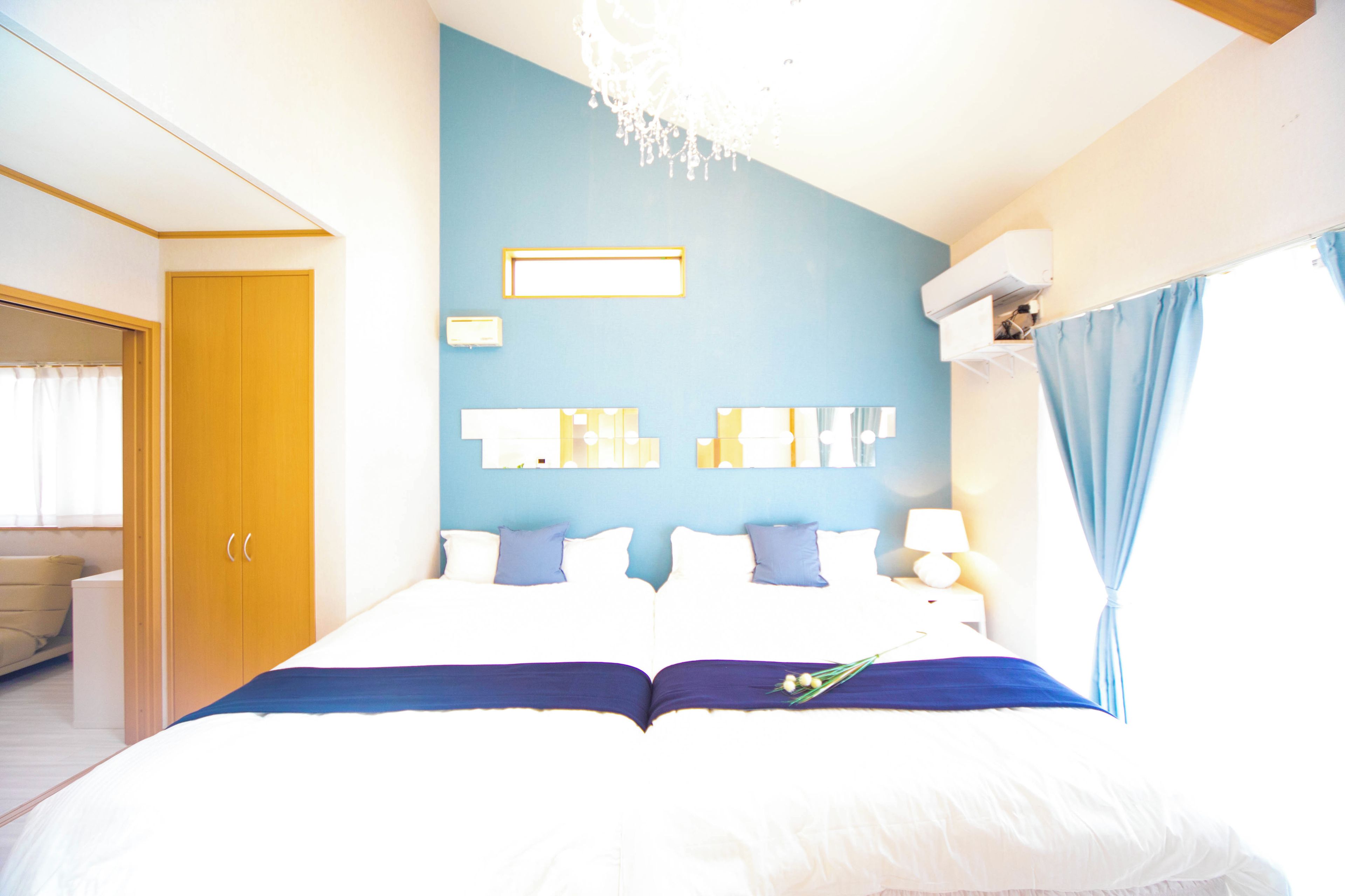 A bedroom with a large bed, a wardrobe, a chandelier, and a window with curtains.