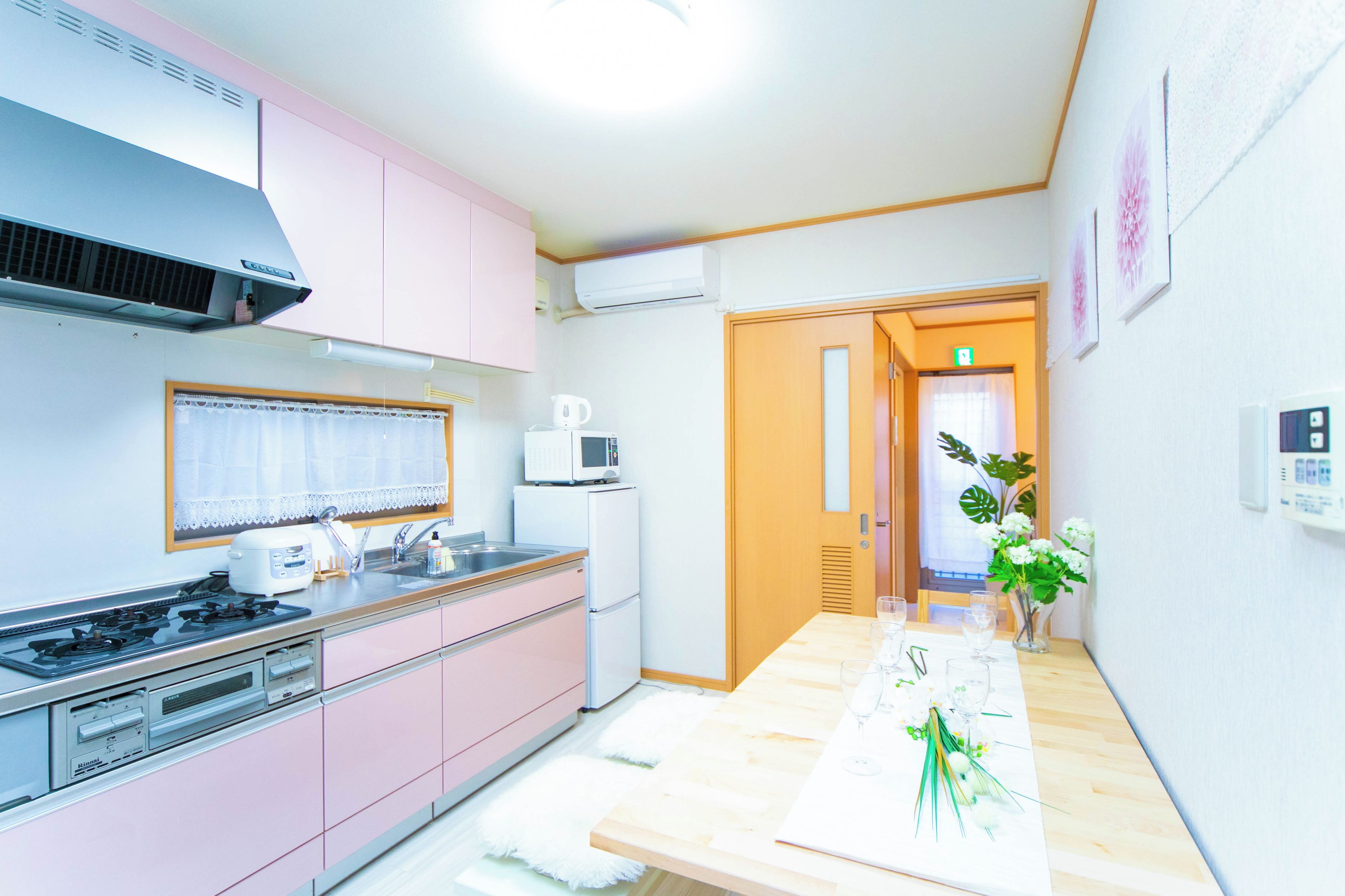 A compact kitchen with pink cabinets, a stove, a microwave, and a refrigerator.