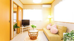 A living room with a sofa, a television, a small table with a vase, and a window with blinds. - Awaji Central Inn Kuruma713 (Awaji)