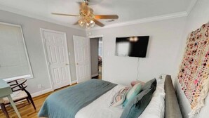 A bedroom with a bed, a desk, a chair, a ceiling fan, and a TV on the wall. - The Wayfarer (Lubbock)