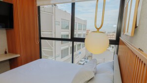 Hotelkamer met een bed, een aan de muur bevestigde televisie en een raam met uitzicht op gebouwen.