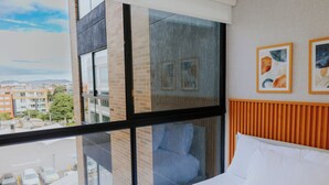 Een hotelkamer met een groot raam, een bed met witte lakens en twee ingelijste kunstwerken aan de muur.