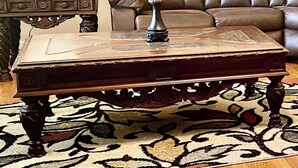 Un salón con un sofá de cuero marrón, una mesa de centro de madera con un objeto decorativo, una lámpara y un cuadro en la pared.