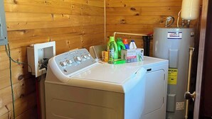 Un lavadero pequeño y funcional con lavadora y secadora de carga frontal, calentador de agua y un armario con productos de limpieza.