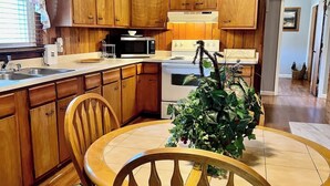 Una cocina con armarios de madera, microondas, estufa y una mesa de comedor con sillas.