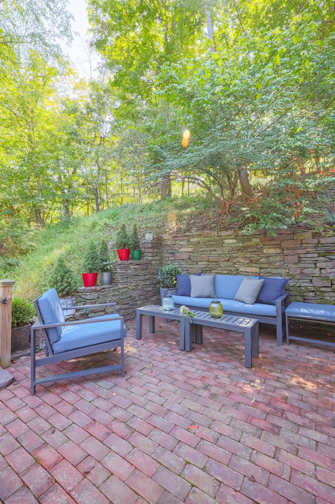 A patio area with a stone wall, a blue sofa, a chair, and a table.