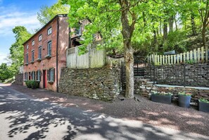 A brick building with a stone wall, a wooden fence, and a tree in front.