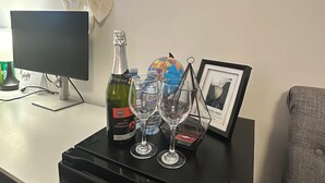 Et skrivebord med en computer, en flaske vin, to vinglas, et indrammet billede og dekorative vægspejle.