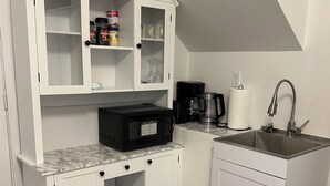 Et kompakt køkken med hvide skabe, en marmor bordplade, kaffemaskine og vask.