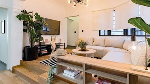 Een moderne woonkamer met een bank, een salontafel, een televisie en een trap naar een andere kamer.
